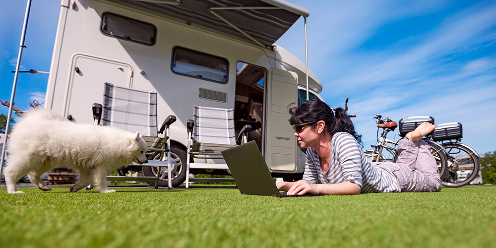 Woman on the grass with a dog looking at a laptop. Caravan car Vacation. Family vacation travel, holiday trip in motorhome VR